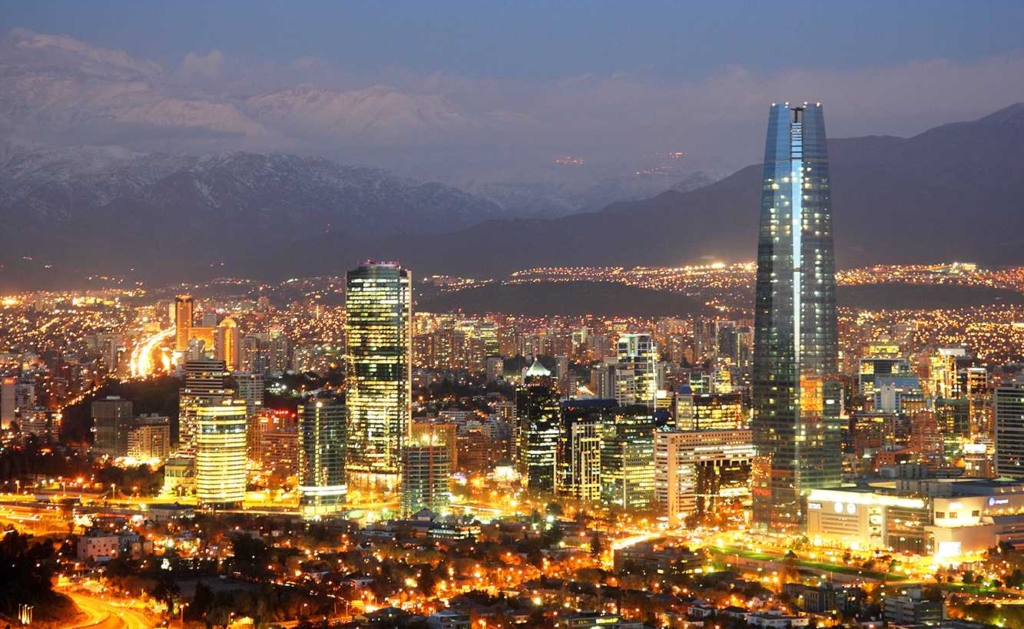 aerial view of a bustling downtown city at night with bright skyscrapers surrounded by mountains in Santiago, Chile