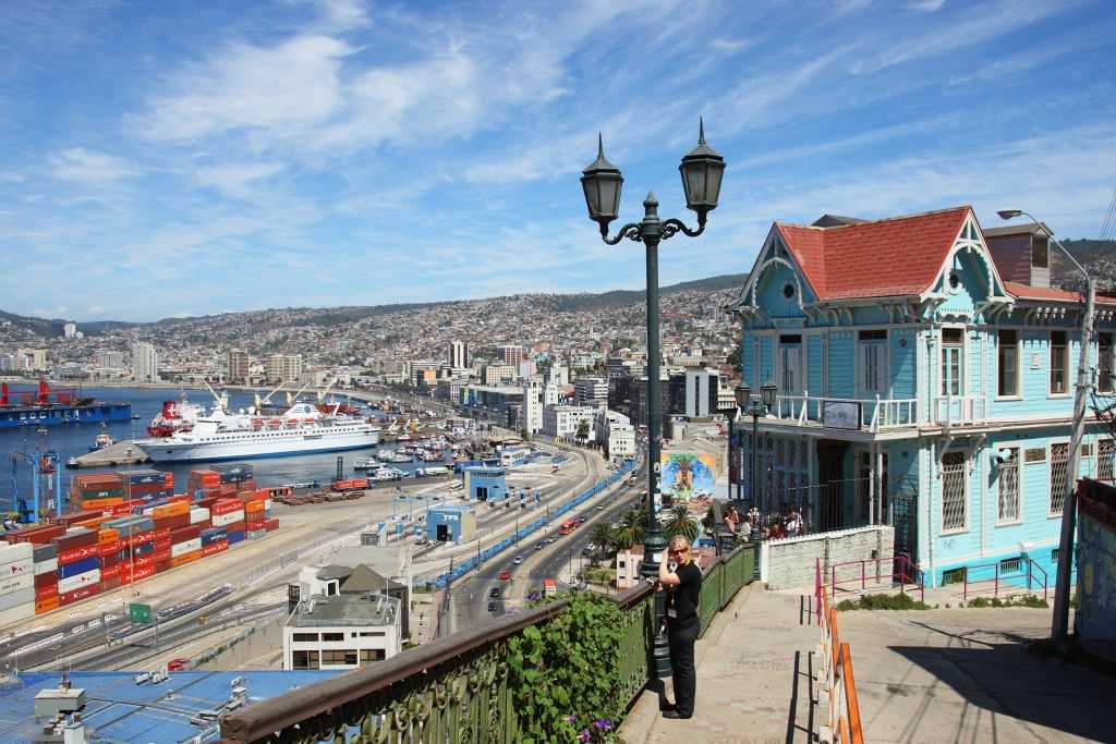 woman standing near a colorful building overlooking a bridge to a ship port in Valparaiso, Chile, South America