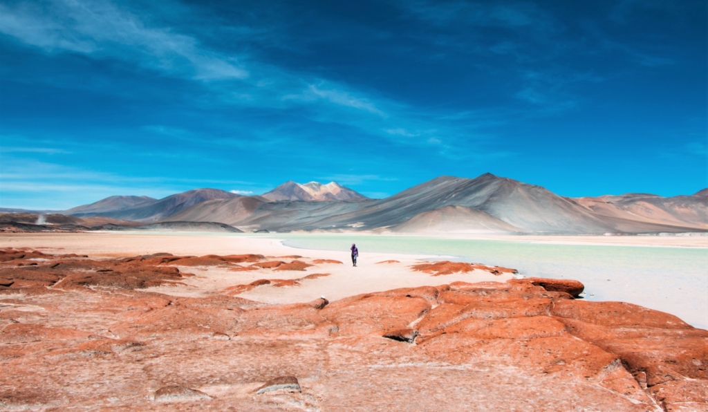 person standing by warm rocks in San Pedro de Atacama Desert in Chile before a vast salt lagoon surrounded by mountains in the background
