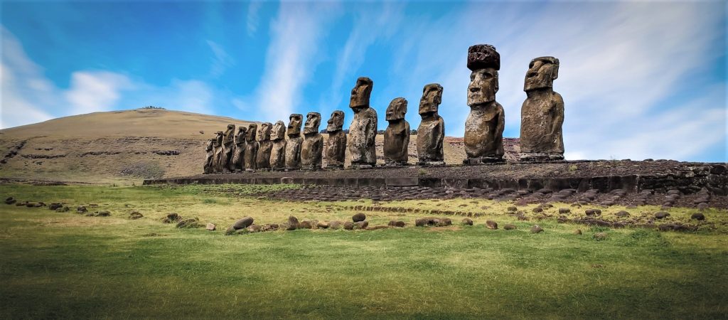 row of towering stone statues on a grassy island with blue, cloudy skies in South America