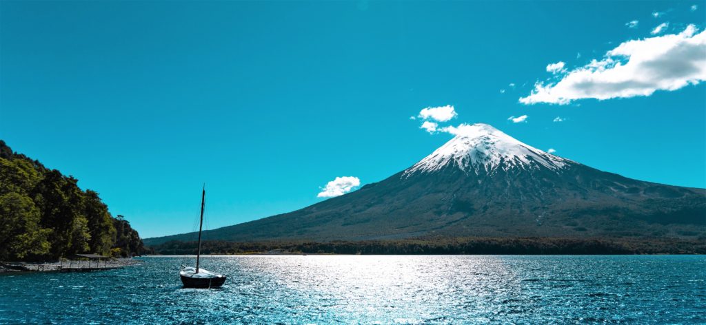 snow-capped volcano near a glistening body of water with a sailboat in Chile