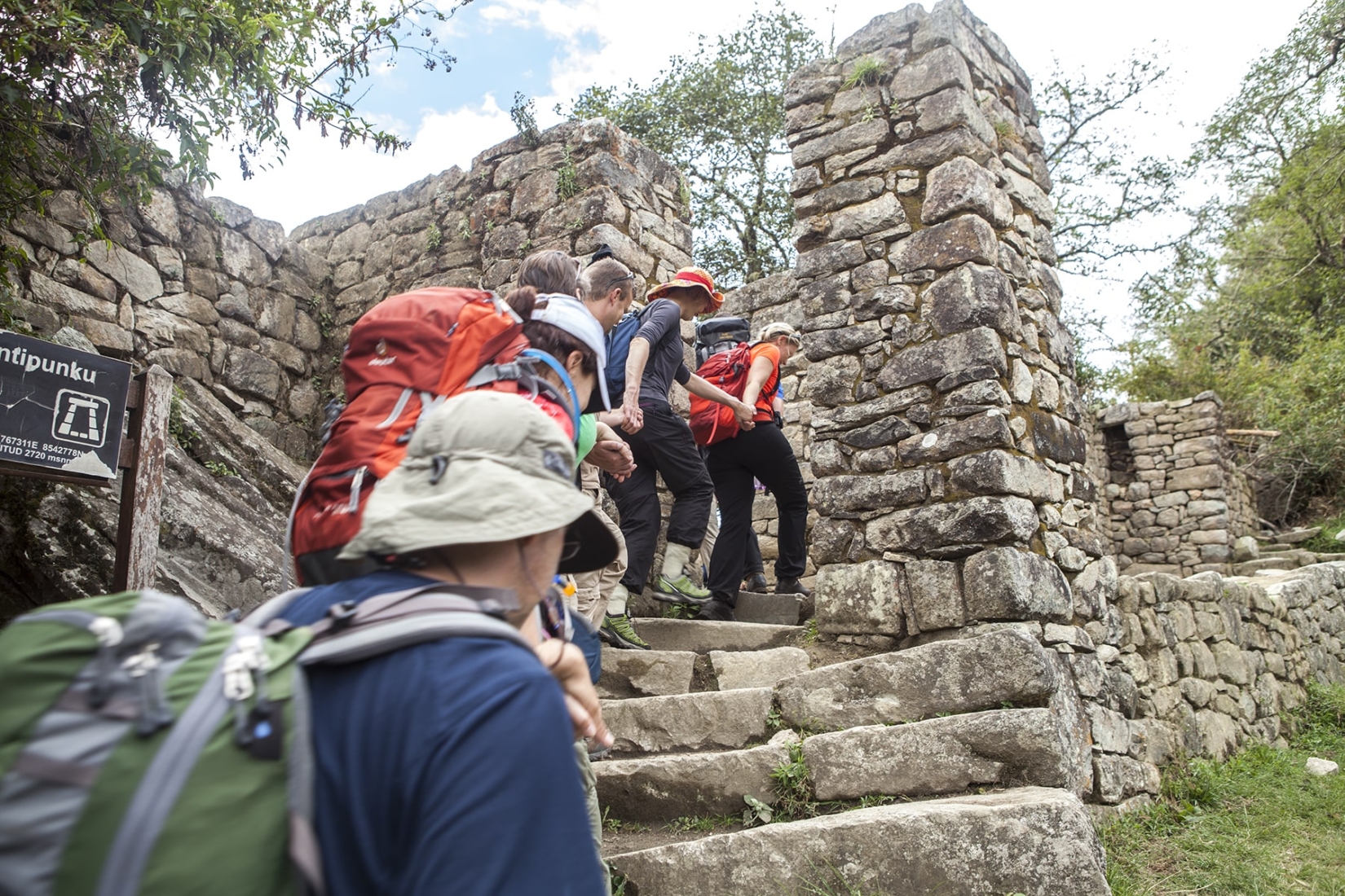 A group of hikers hold hands as they walk through a gateway to reach Machu Picchu on an Inca Trail tour with The Explorer’s Passage