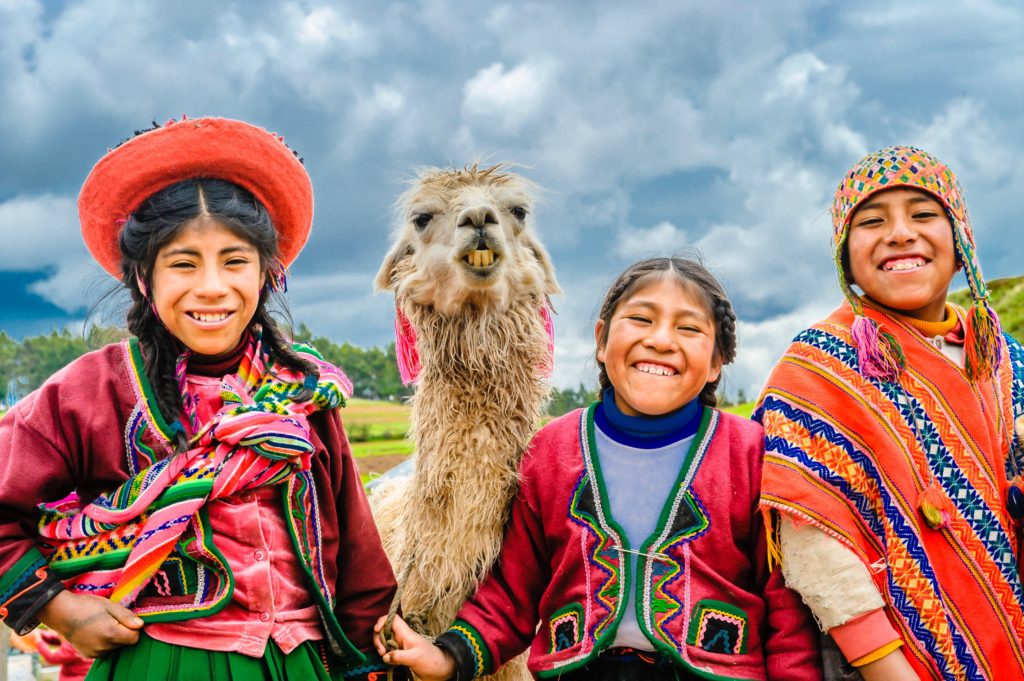 Smiling Peru kids in colorful traditional woven clothes with an alpaca