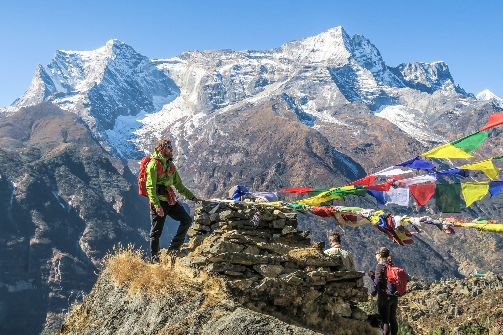 Trekker with backpack standing on rocks next to prayer flags while gazing at snow-capped mountains in Nepal