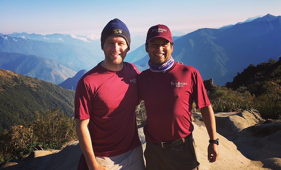 A photograph of two men wearing maroon t-shirts in the mountains of Peru’s Sacred Valley, on an Inca Trail tour. One man is a trekker and the other is a local guide