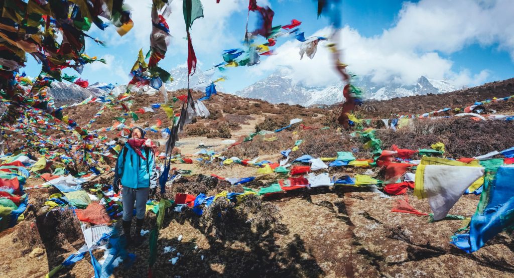 Woman trekker looking up at the blue sky and surrounded by colorful prayer flags in the wind on Everest Base Camp.