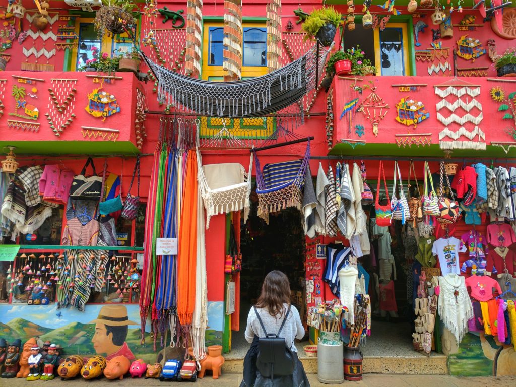 Solo female traveler standing in front of a red building shop decorated with local crafts and bags.