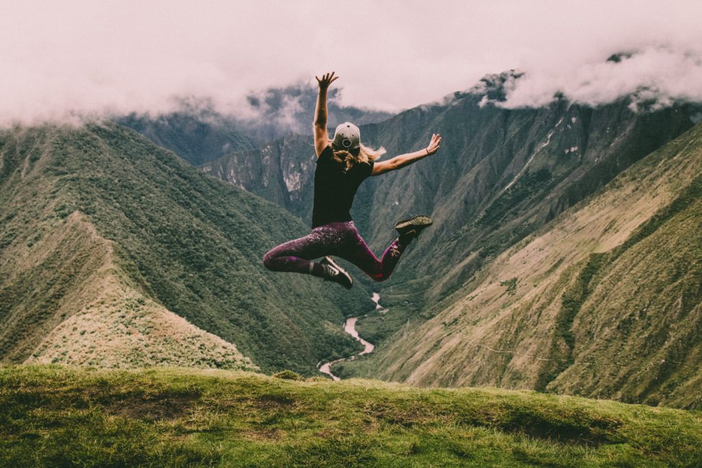 Woman jumping on the Inca Trail in between the green Andes Mountains.
