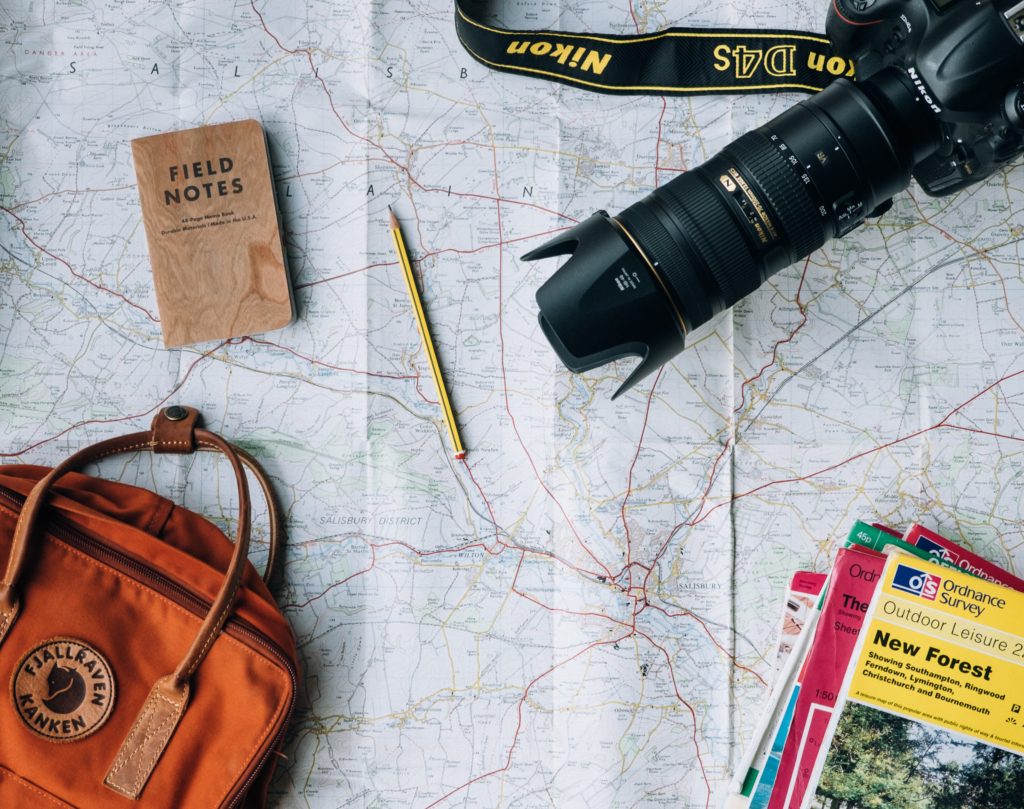 Layout of maps, a camera, bag, and notebook for trip planning.