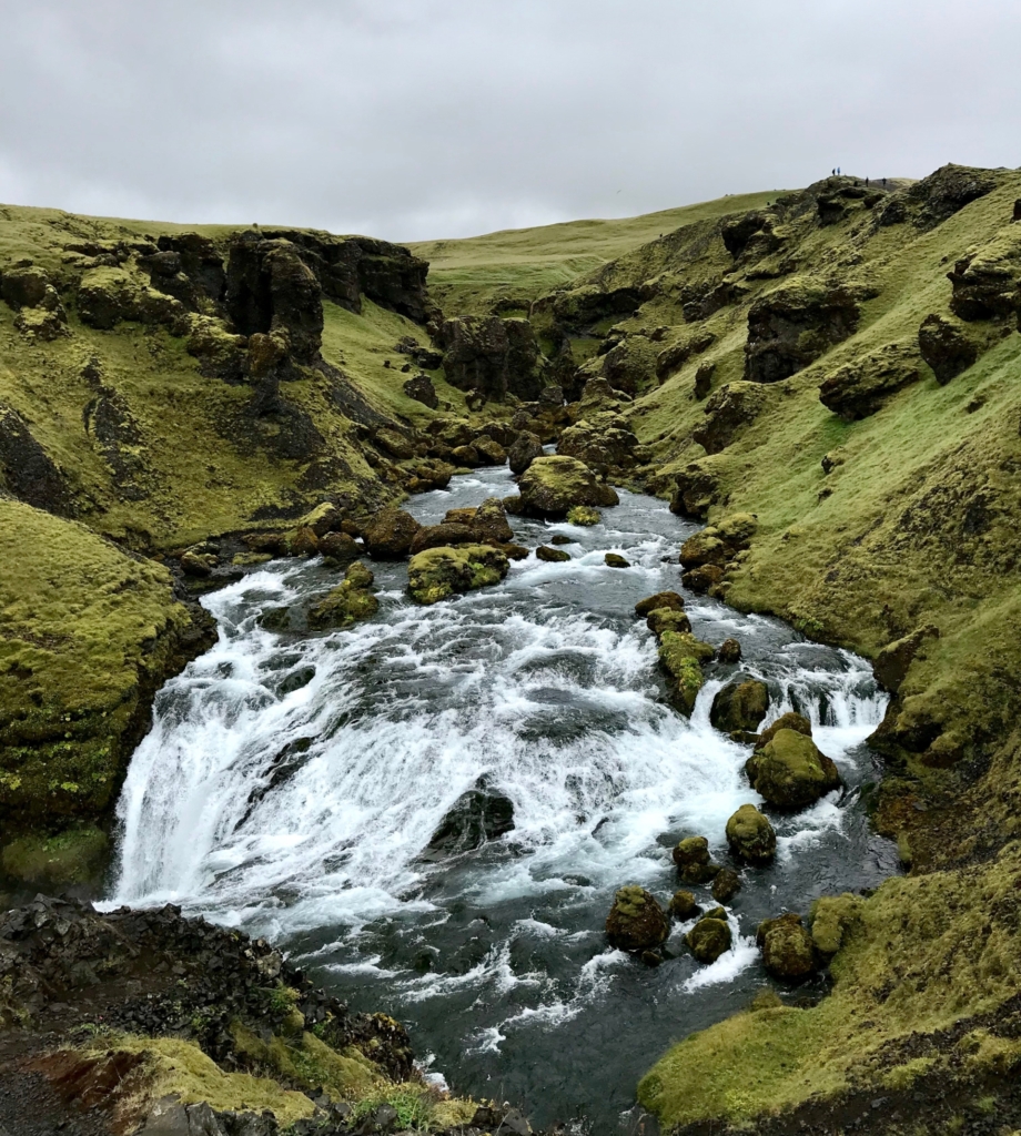 Mossy lush glacial valley trail in Iceland with water flowing through rocky river bed