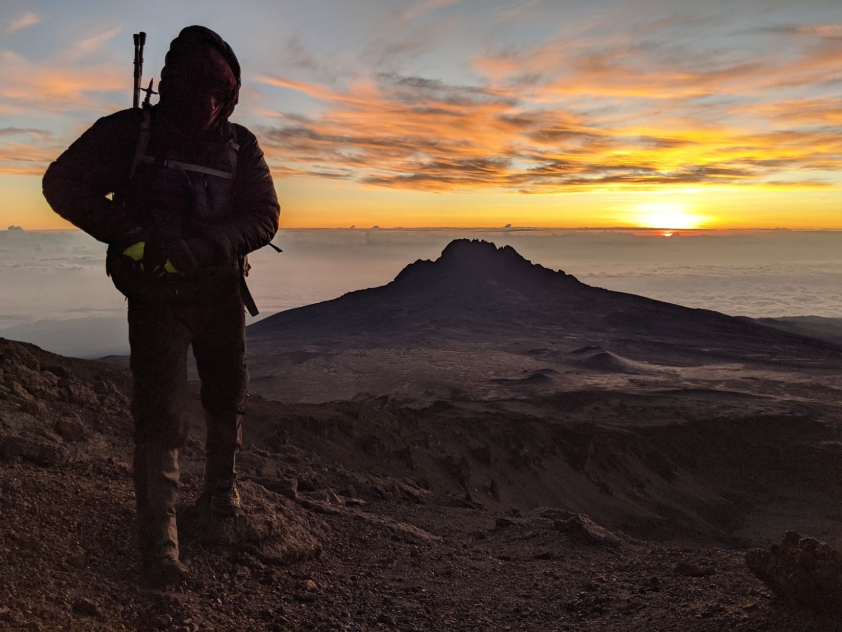 Man in black jacket and pants standing on top of Kilimanjaro during sunrise 