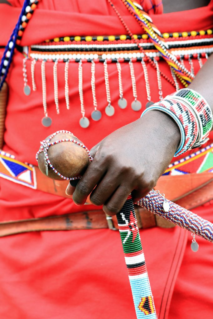 African tribe member holding a colorful beaded stick and wearing traditional clothing and jewelry
