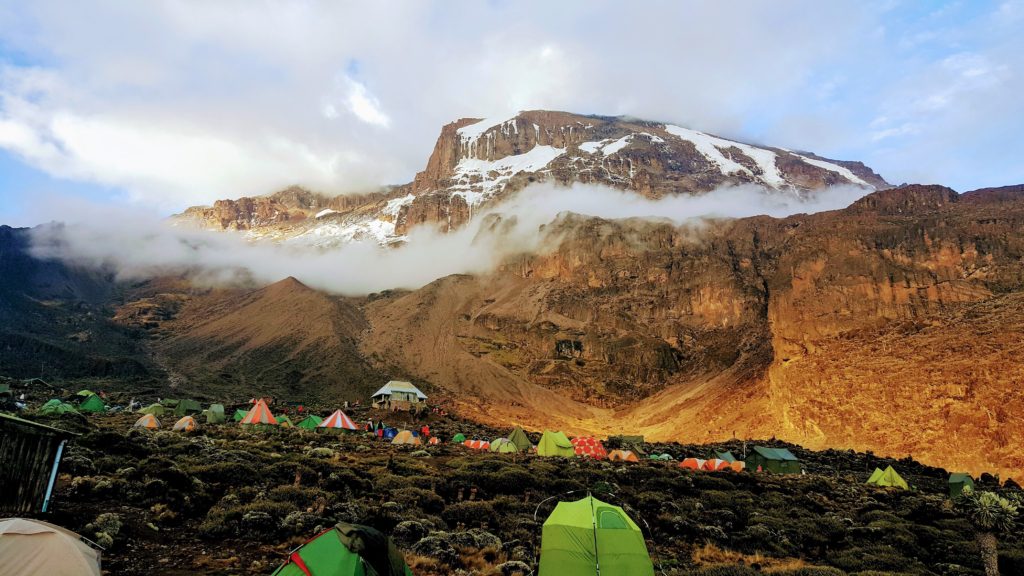 Barranco Wall. Colorful tents scattered on rocky terrain at the base of an African mountain on a cloudy day on the Machame route of Kilimanjaro