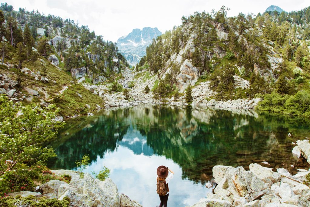 A traveler taking nature photos of a lake and its reflection of green mountains