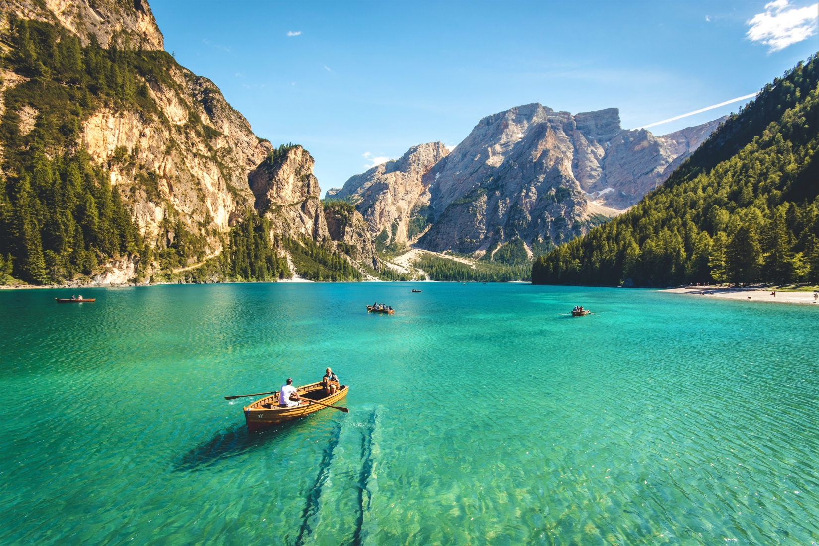 People traveling sustainably in wooden row boats floating on a clear turquoise lake surrounded by green mountains on a sunny day