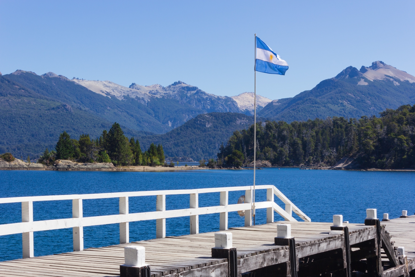 Argentinian flag waving over a dock on a lake with mountains in background