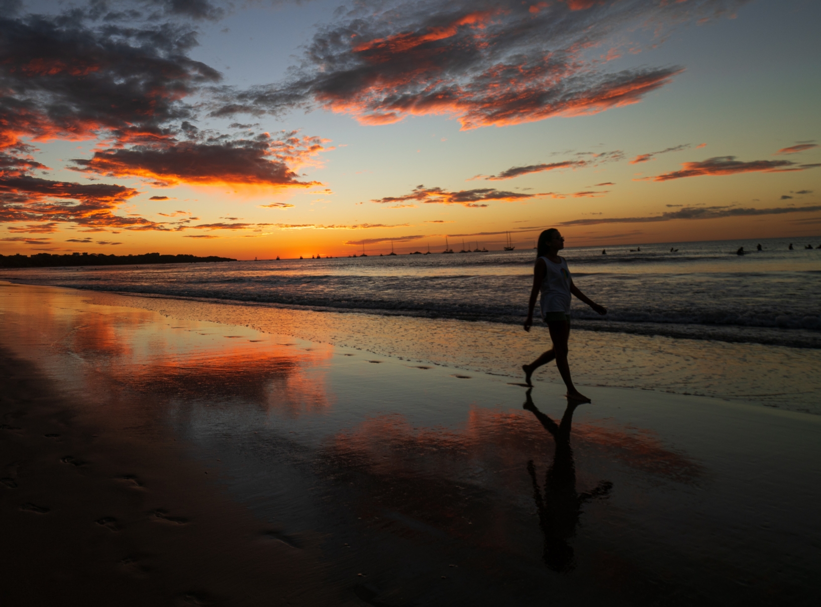 A woman walks along the beach at sunset as vibrant hues paint the sky