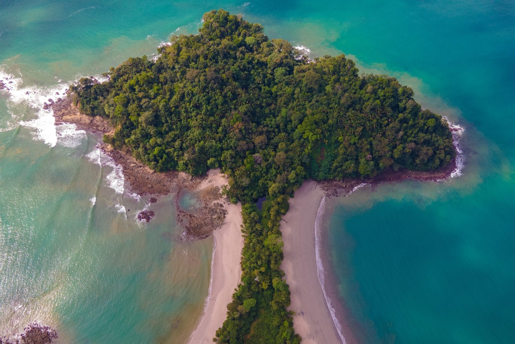 Mushroom-shaped peninsula filled with dense greenery with beaches outlining the stalk and turquoise waters surrounding the cutout