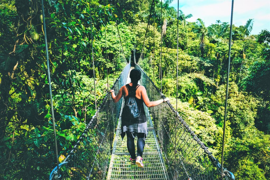 Woman with backpack walking across canopy bridge in cloud forest