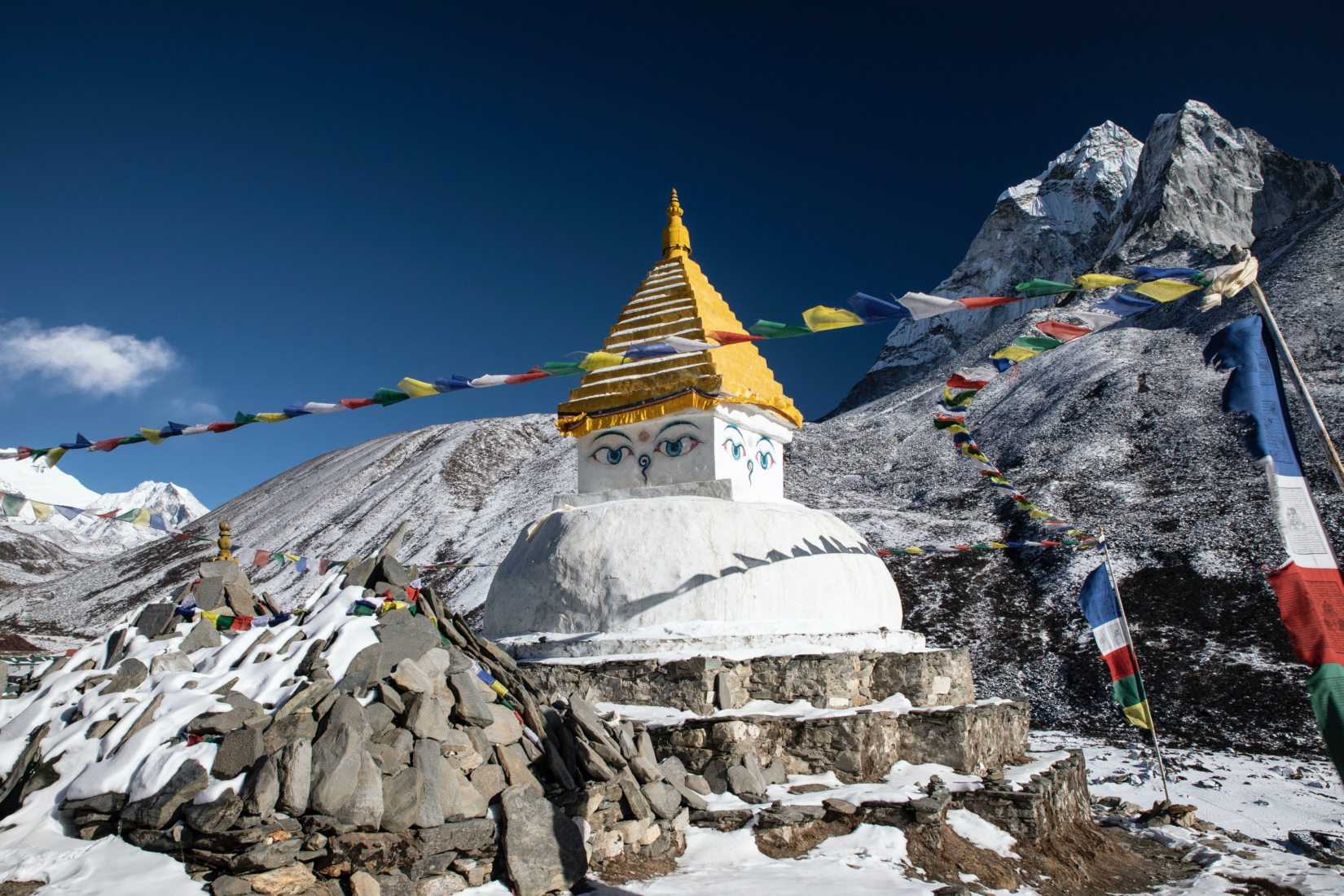 A stupa with eyes and a golden top, with strings of prayer flags, surrounded by mountains near Dingboche in Nepal