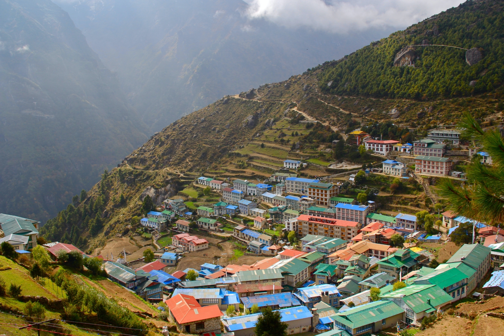 A photograph of Namche Bazaar, a market town and primary trading hub on the trail to Everest Base Camp in Nepal. The town of Namche Bazaar is built into the hillside