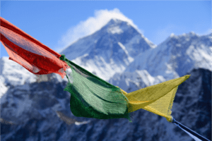 A photograph of colorful prayer flags fluttering in the wind, with Mount Everest in the background