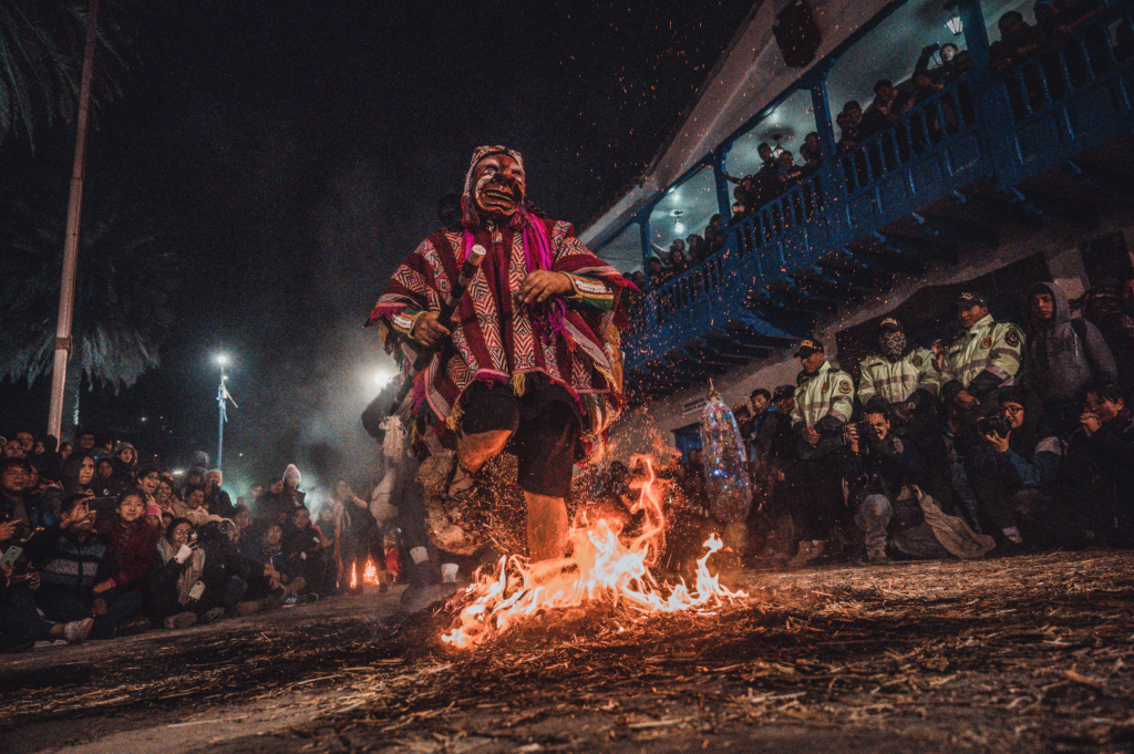 Costumed dancer stomping on flames on the street during Paucartambo Festival