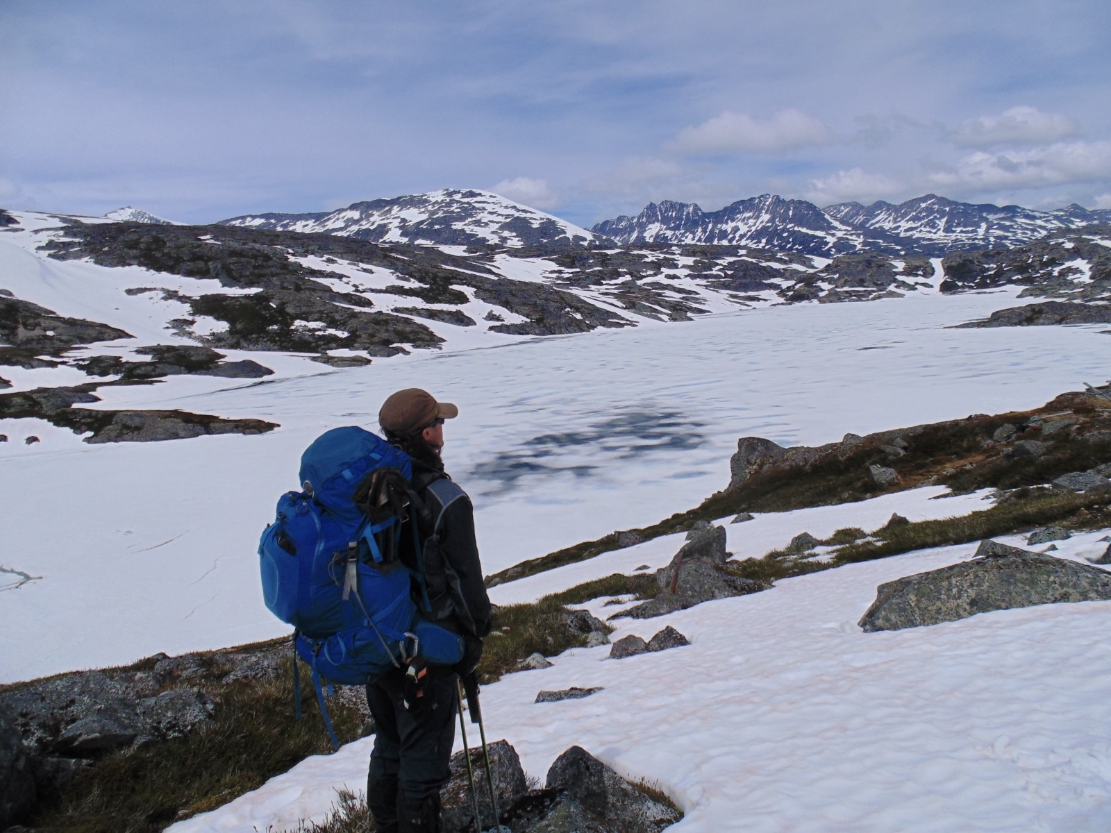 A hiker with a backpack looks out over snow-capped Coast Ranges