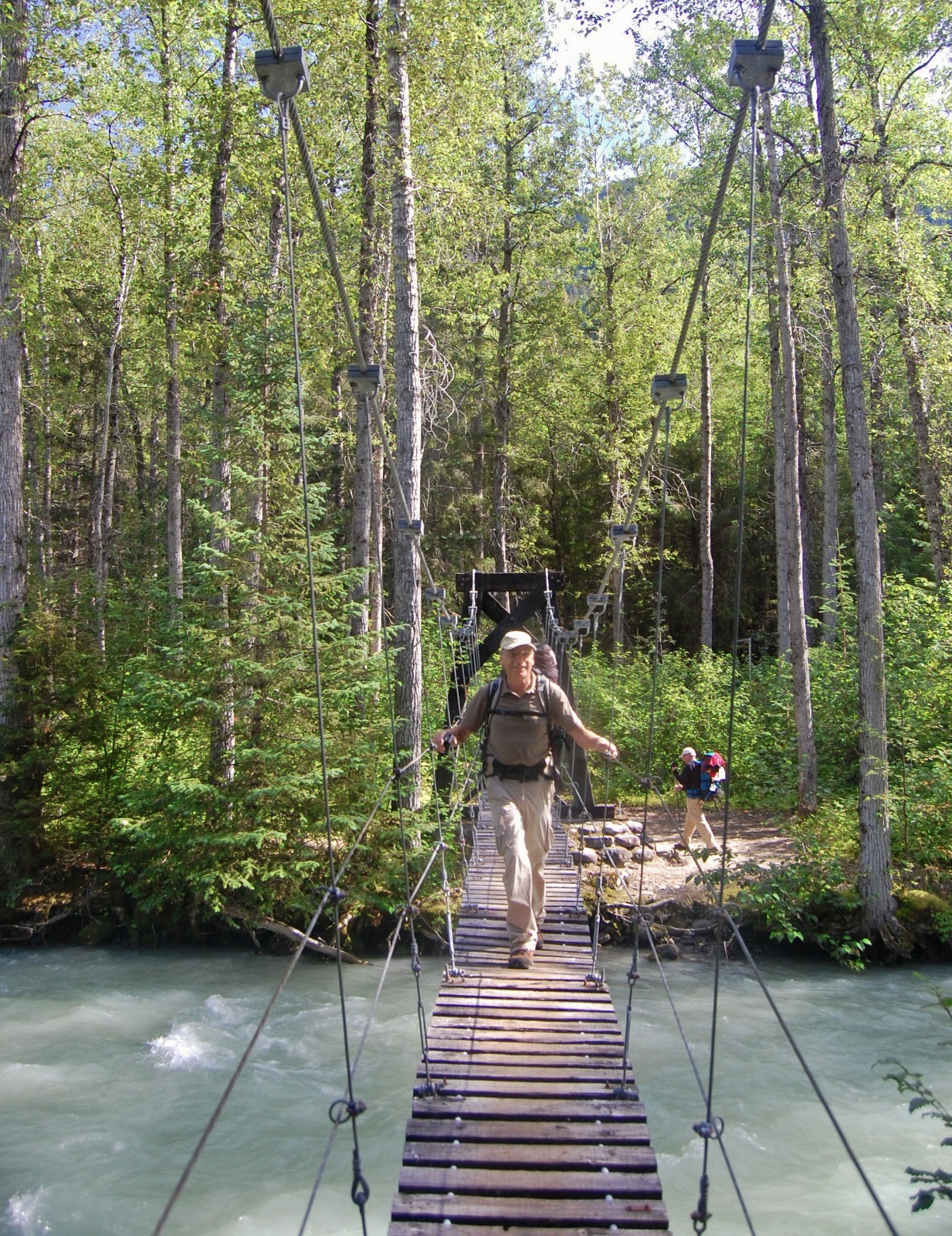 A hiker crossing a hanging bridge over a river along the Chilkoot Trail hike