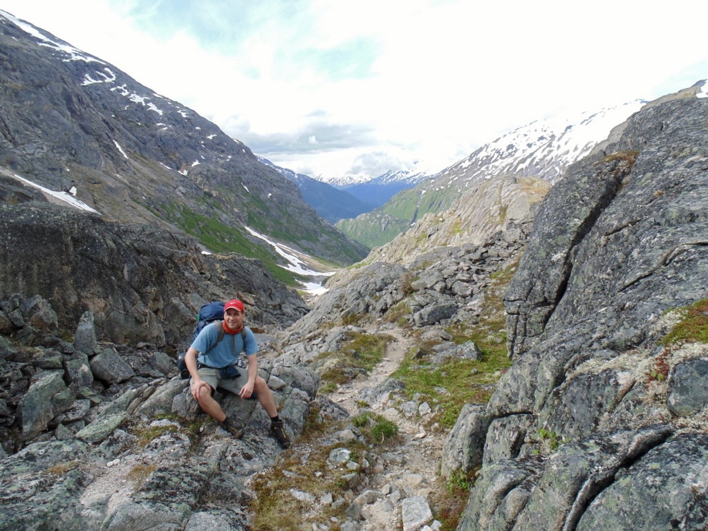 A hiker sitting on rocky terrain in a valley of the Chilkoot Trail hike