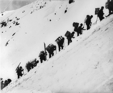 Gold Rush prospectors with supplies hiking the snowy Chilkoot Pass in 1898